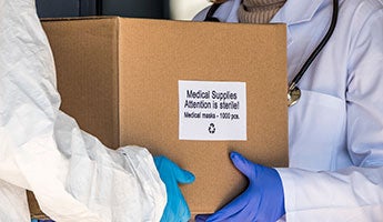 a person with gloved hands handing a box of medical supplies to another person with gloved hands
